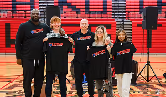 A group of people gathered holding shirts and smiling for the camera