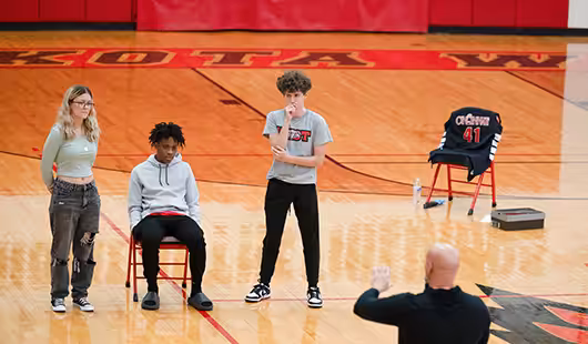 Three students on the gym floor listening to the speaker